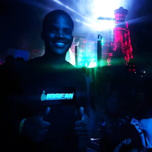 Man smiling with two thumbs up wearing custom company light up t-shirt illuminating brightly in festival setting